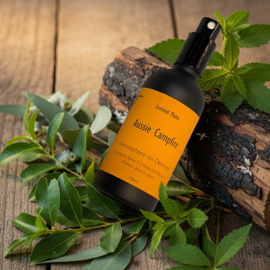 A minimalist matte black room spray bottle with a vibrant orange label, placed among charred natural wood and dried eucalyptus leaves.