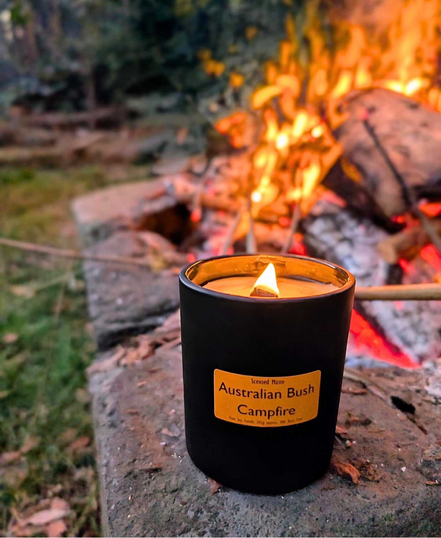 A lit wooden wick candle on a stone with a campfire and trees in the background