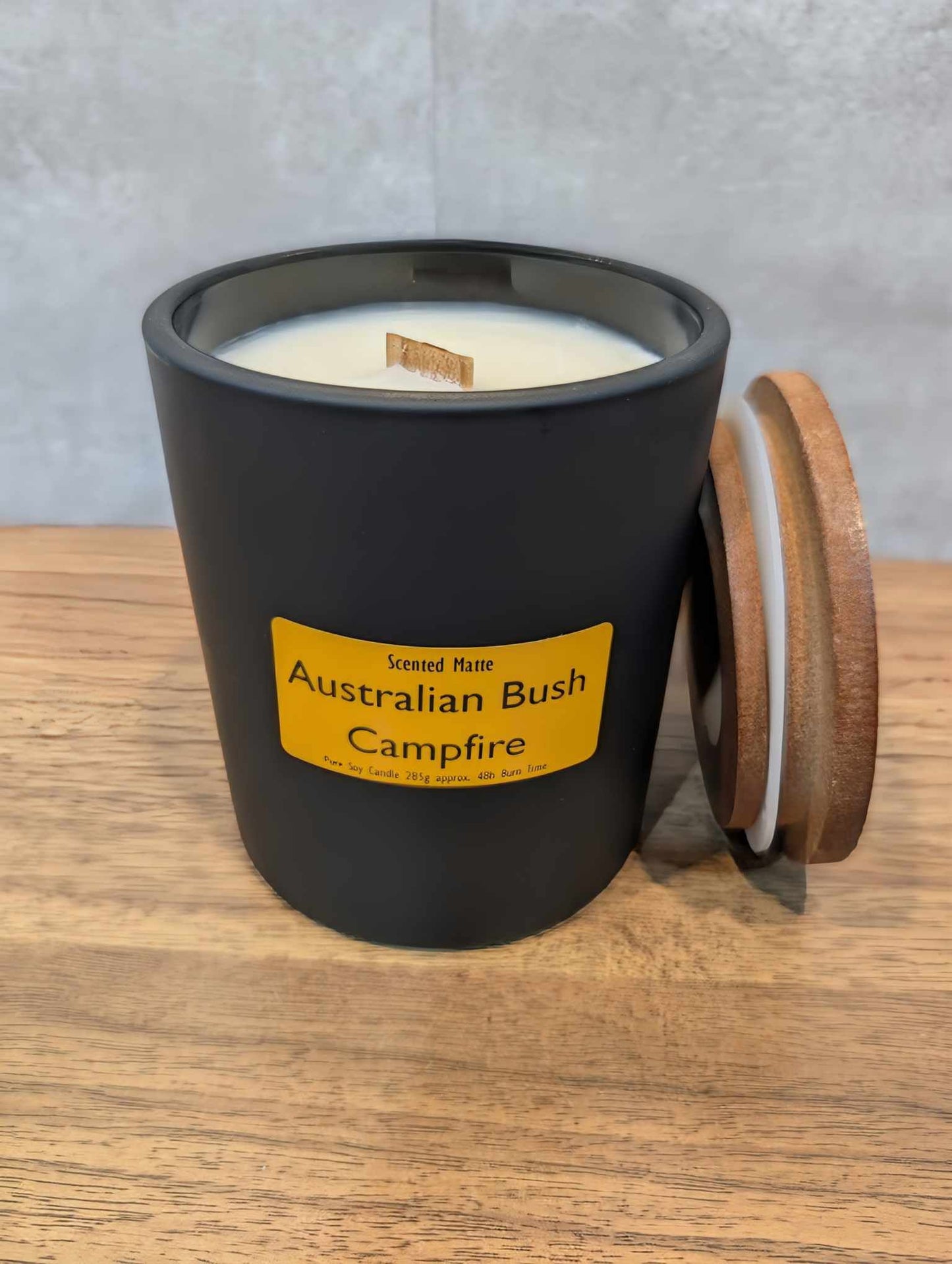 A soy wooden wick candle in a matte black glass jar with an orange label and wooden lid