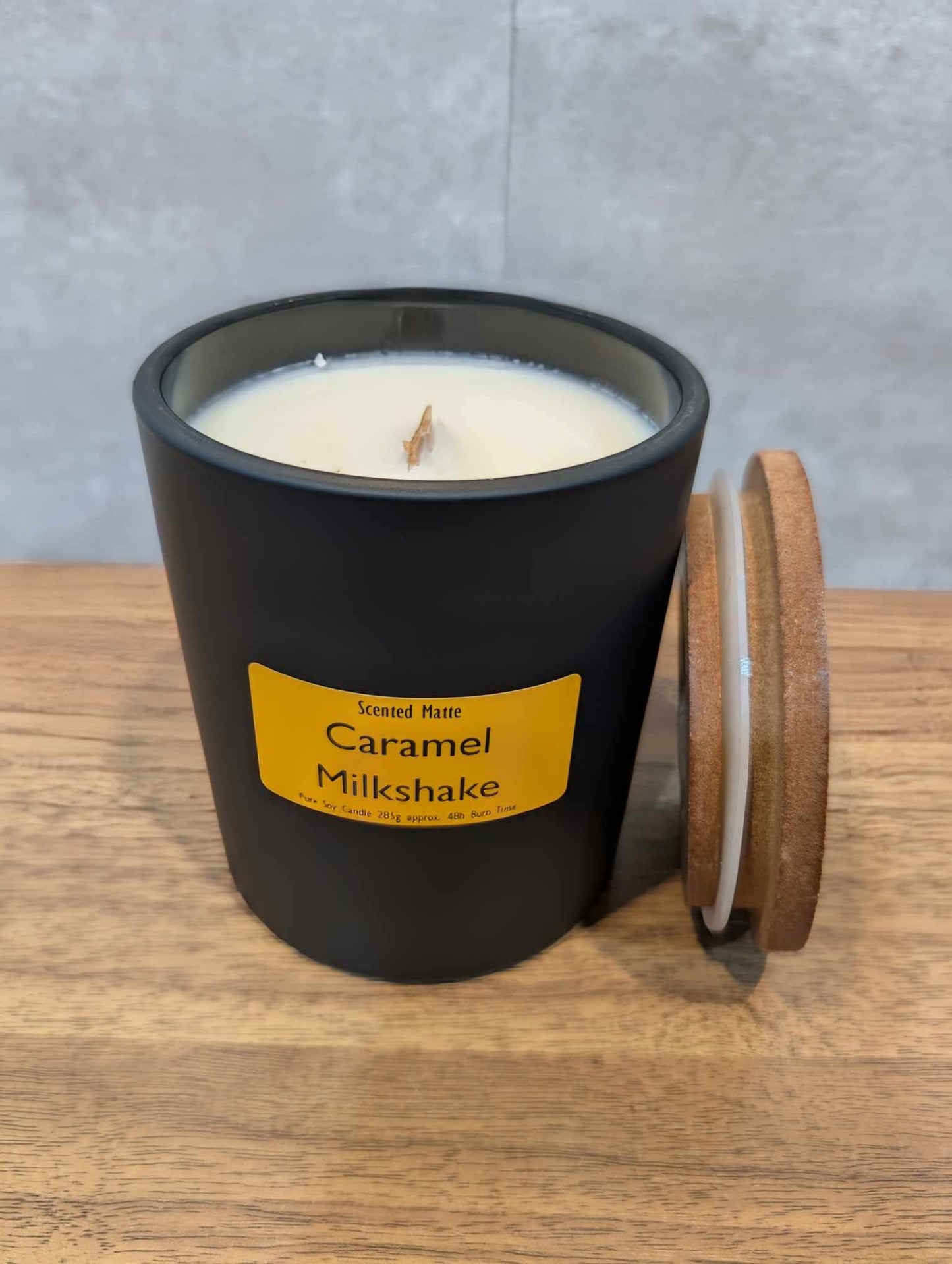 A soy wooden wick candle in a matte black glass jar with an orange label and wooden lid