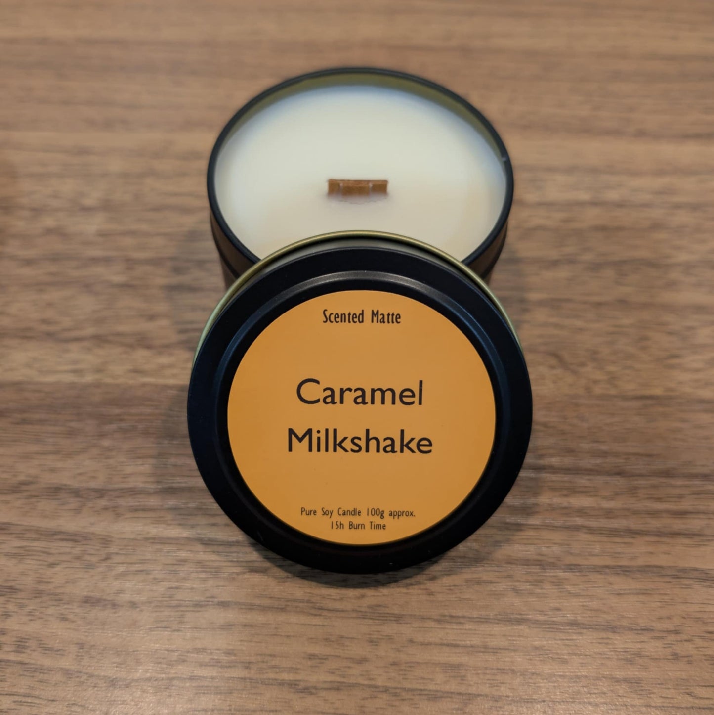 Candle in a tin with 'Caramel Milkshake' label on a wooden surface