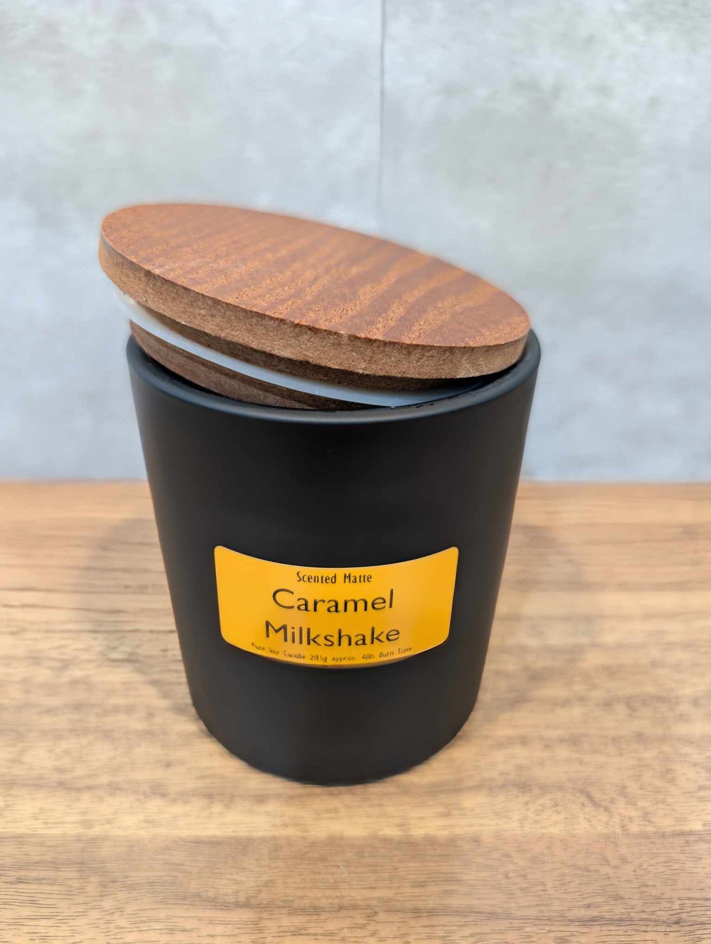 A matte black candle jar with orange label and a wooden lid on top