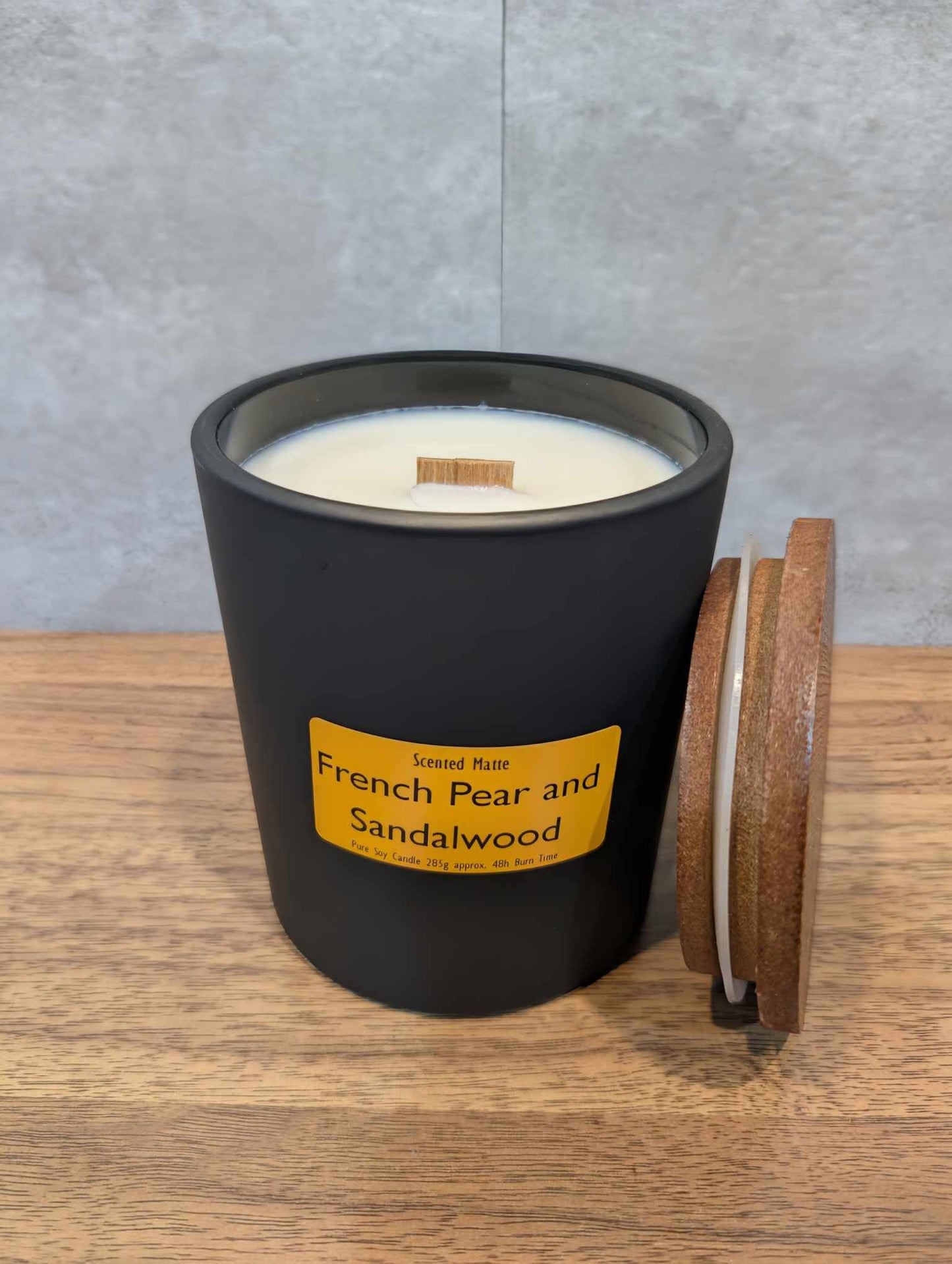 A soy wooden wick candle in a matte black glass jar with an orange label and wooden lid
