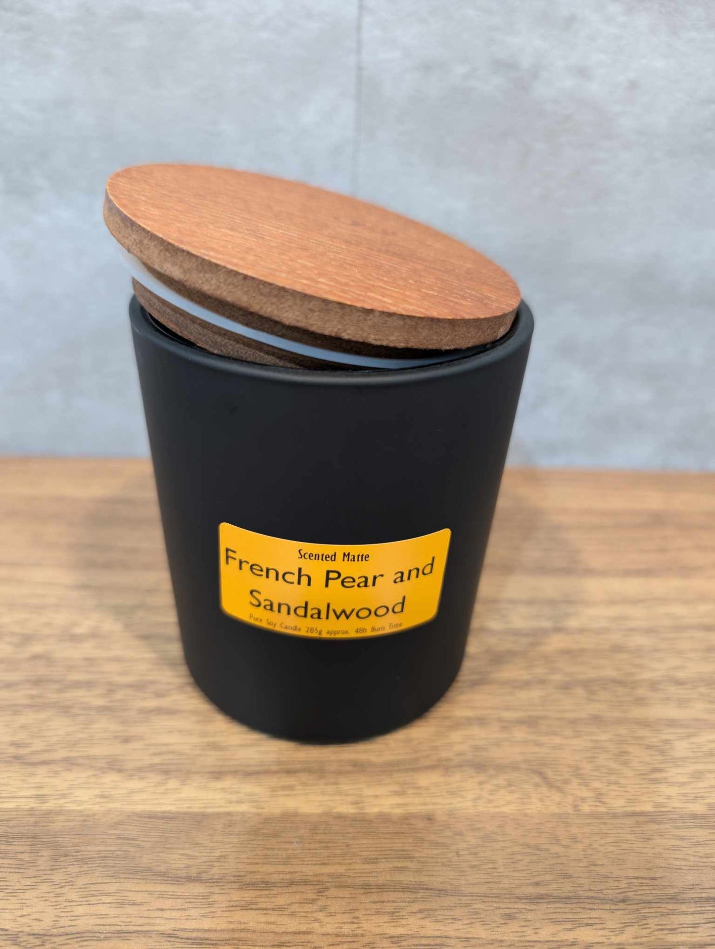 A matte black candle jar with orange label and a wooden lid on top
