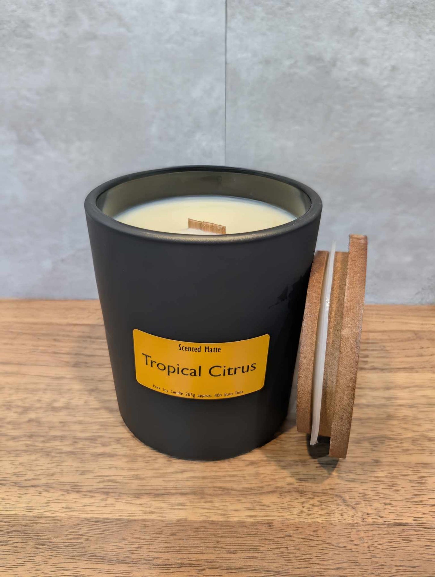 A soy wooden wick candle in a matte black glass jar with an orange label and wooden lid