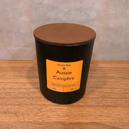 A minimalist matte black candle jar with a vibrant orange label and a dark wood lid.