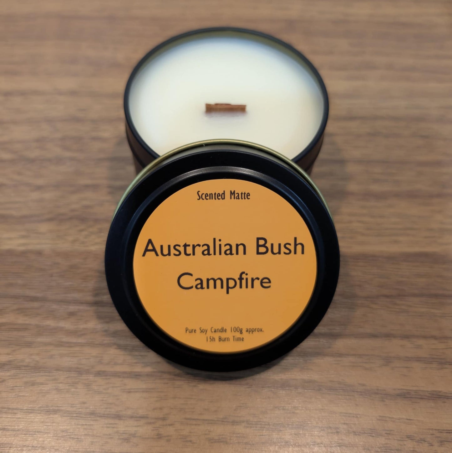 Scented candle in a tin labeled 'Australian Bush Campfire' on a wooden surface