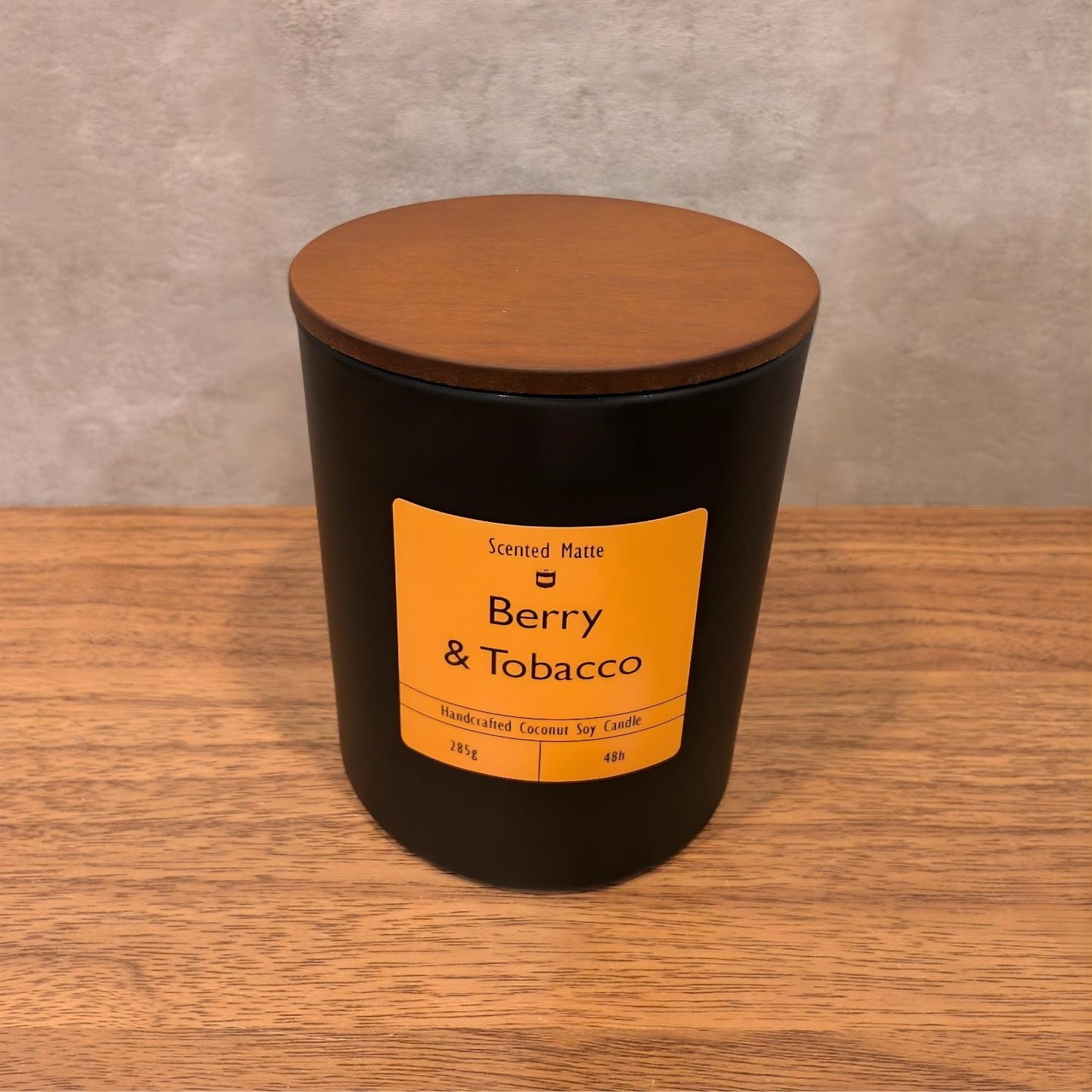 A minimalist matte black candle jar with a vibrant orange label and a dark wood lid.
