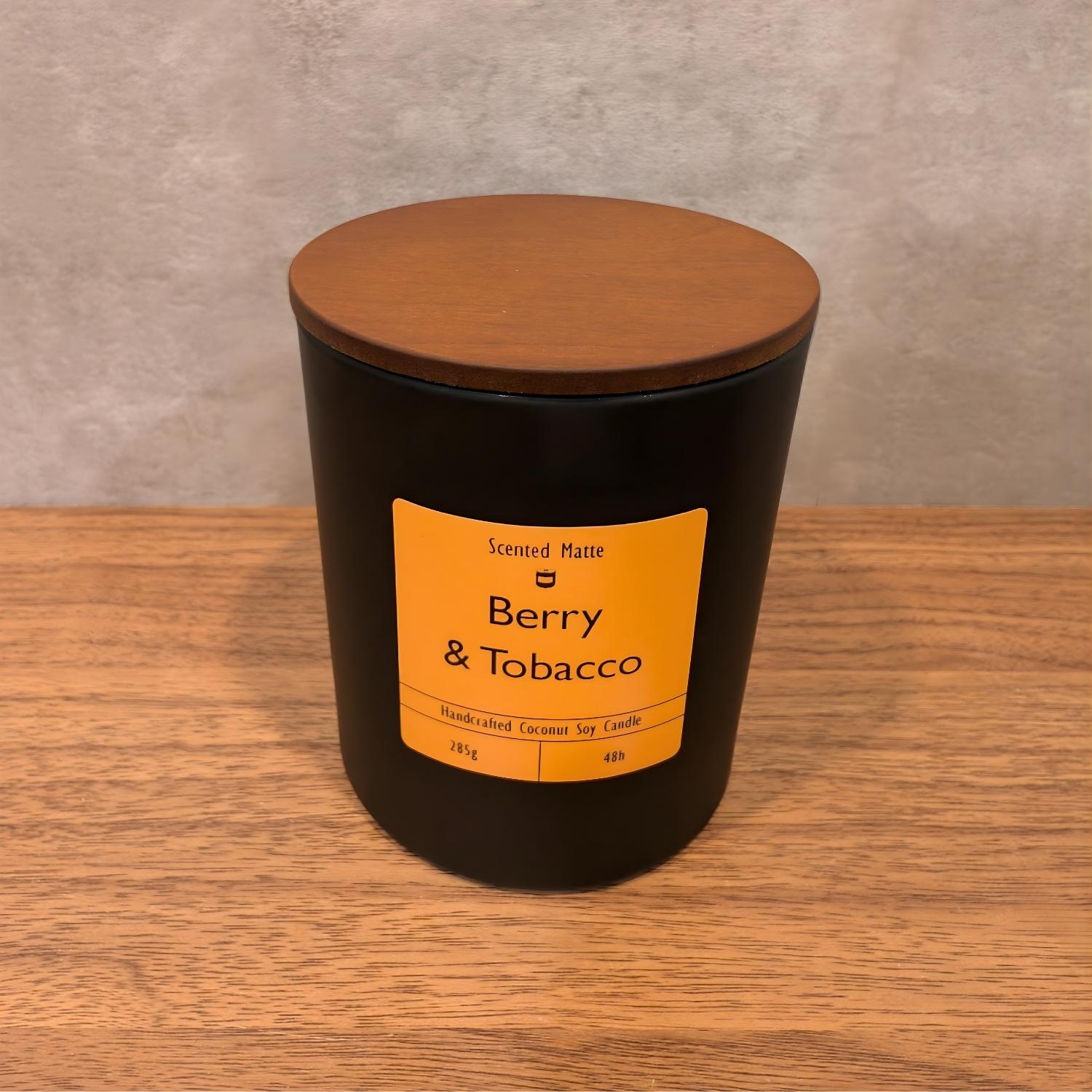 A minimalist matte black candle jar with a vibrant orange label and a dark wood lid.