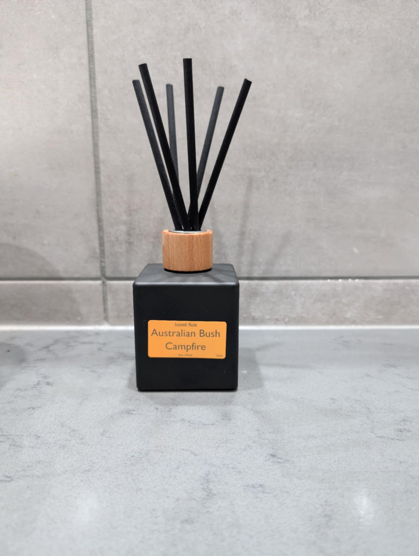Black diffuser bottle with wooden cap and black sticks on a gray surface