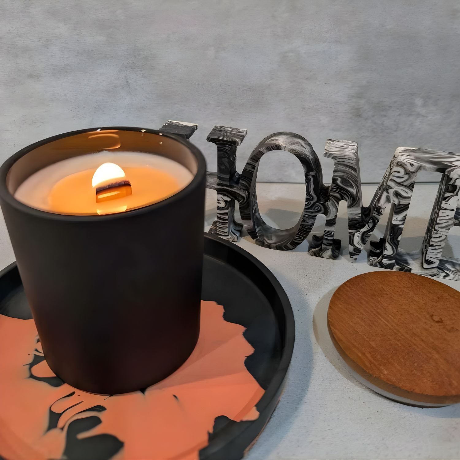 Minimalist matte black candle jar on a decorative tray with 'HOME' letters in the background.