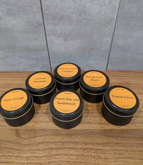 6 candle tins with lids on, showing all different scent labels