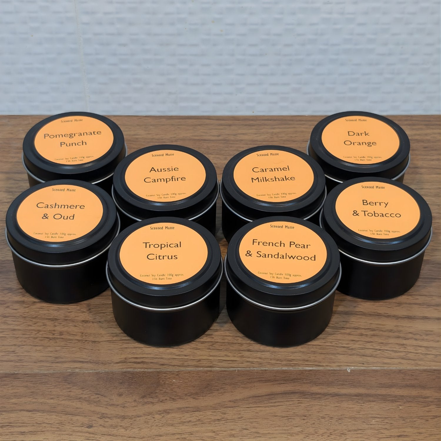 Assorted coconut soy candles in black tins with orange labels on a wooden surface.