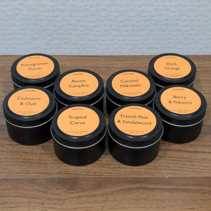 Assorted coconut soy candles in black tins with orange labels on a wooden surface.