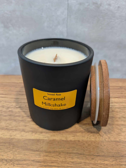 A soy wooden wick candle in a matte black glass jar with an orange label and wooden lid
