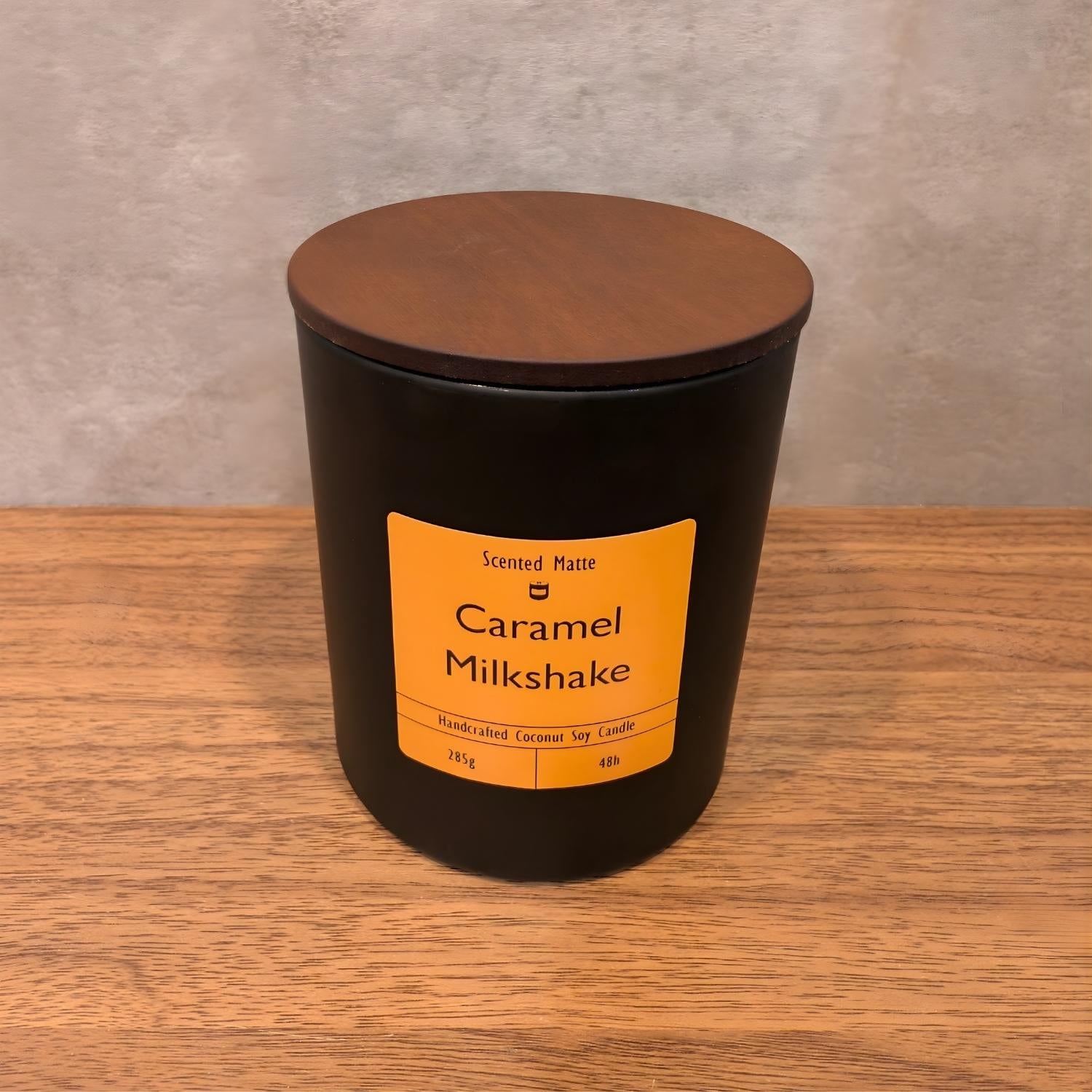 A minimalist matte black candle jar with a vibrant orange label and a dark wood lid.