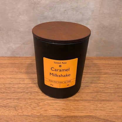A minimalist matte black candle jar with a vibrant orange label and a dark wood lid.