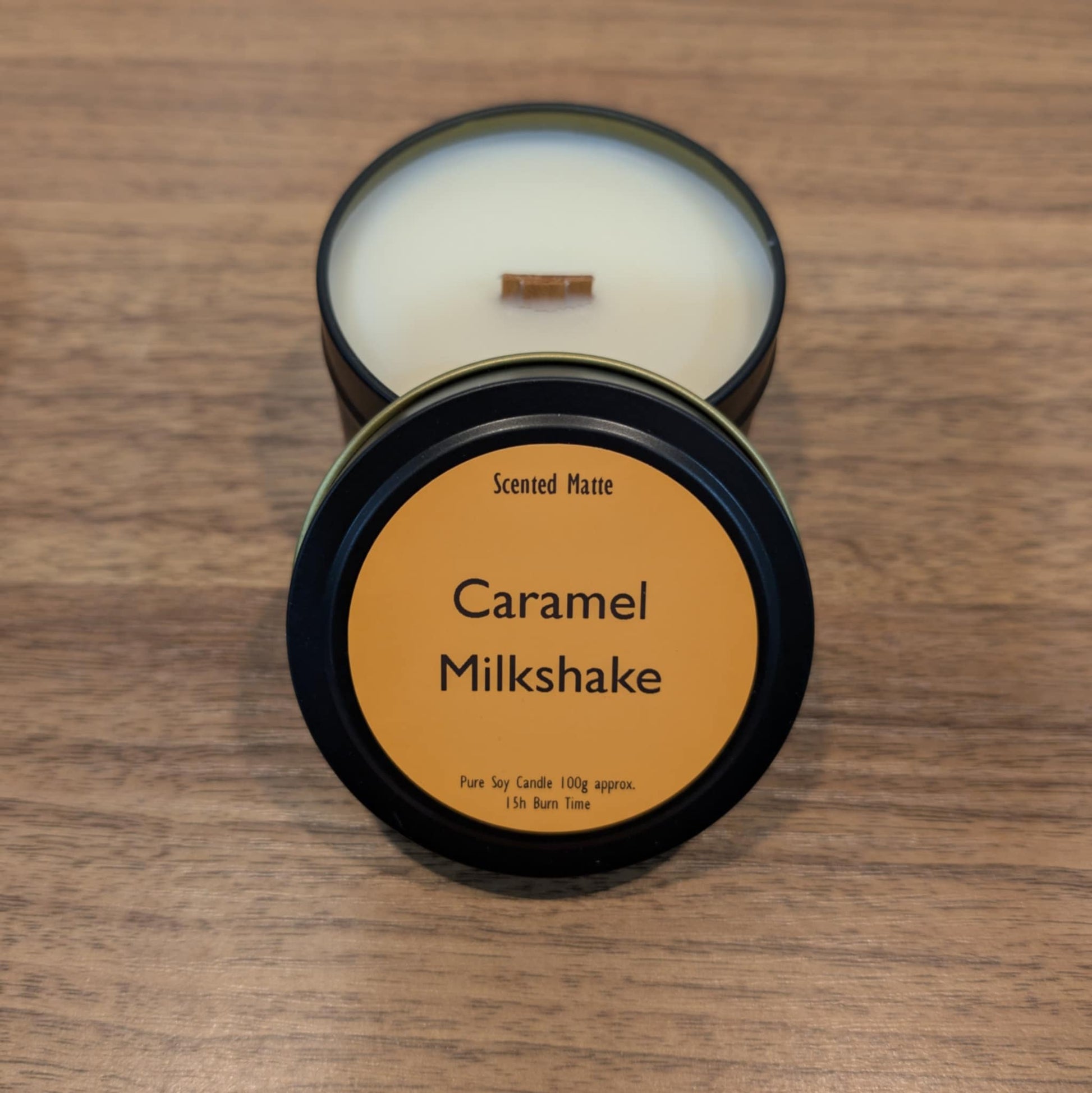 Candle in a tin with 'Caramel Milkshake' label on a wooden surface