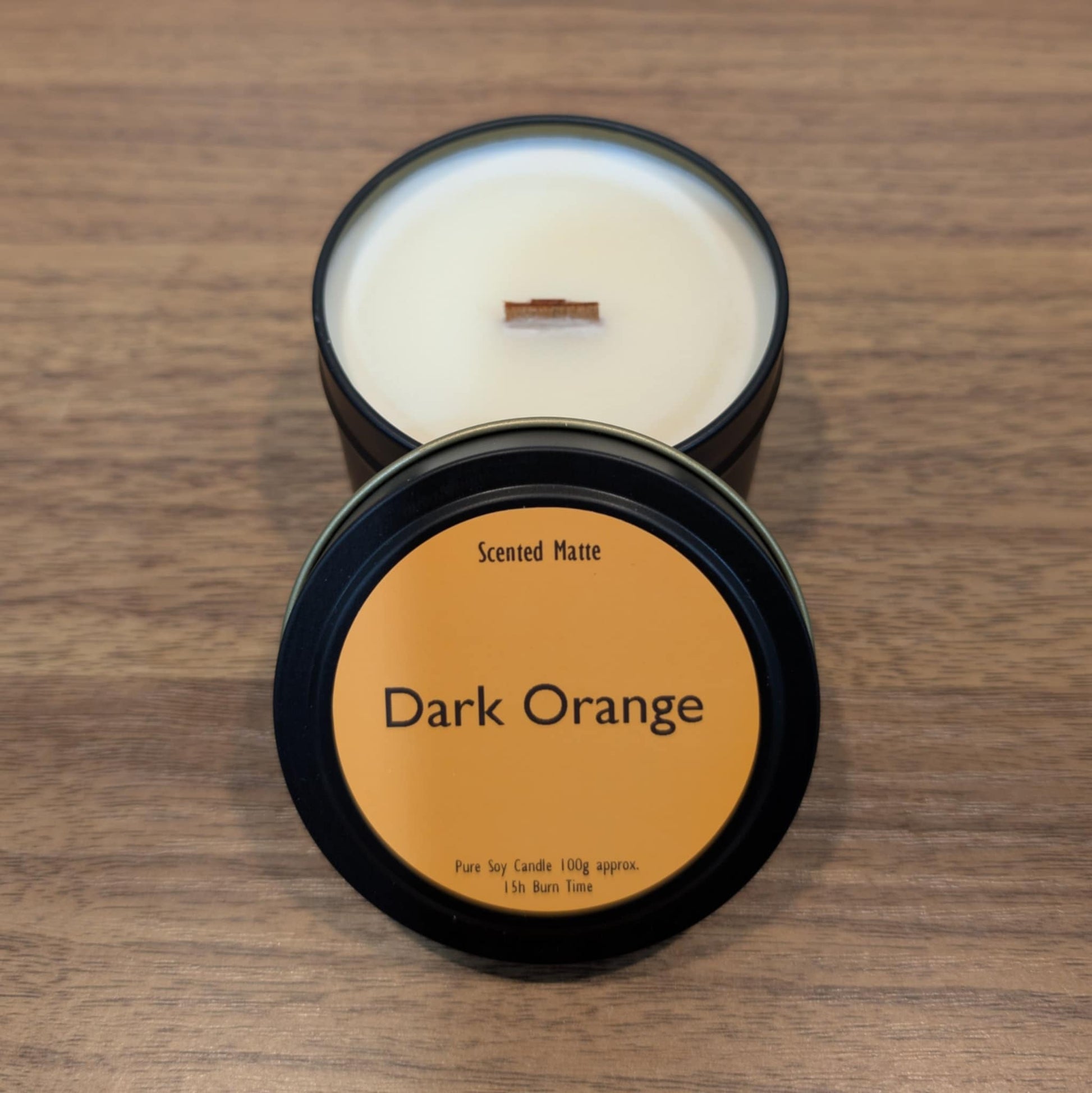 Scented candle in a dark container with 'Dark Orange' label on a wooden surface