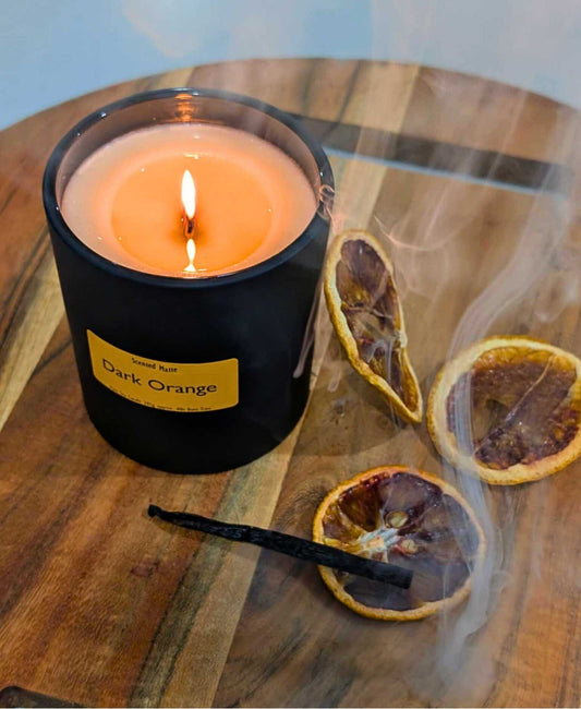 A round board with blood orange slices, a vanilla bean and wisps of smoke next to a lit wooden wick candle