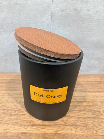 A matte black candle jar with orange label and a wooden lid on top