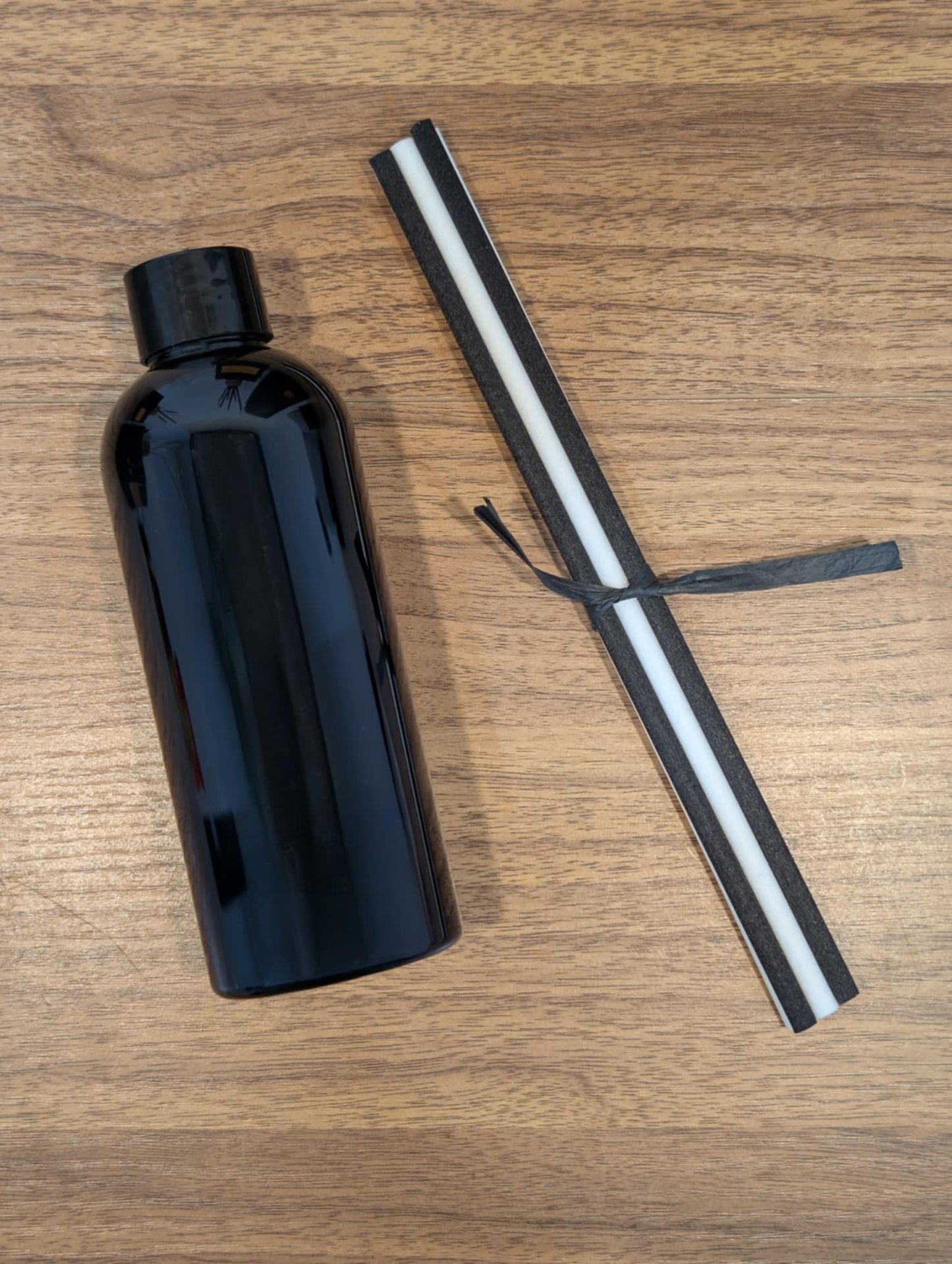 A black bottle with white and black reeds tied with a paper strin on a wooden surface.