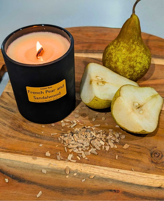 A round wooden board with pear wedges and wood chips with a lit wooden wick candle