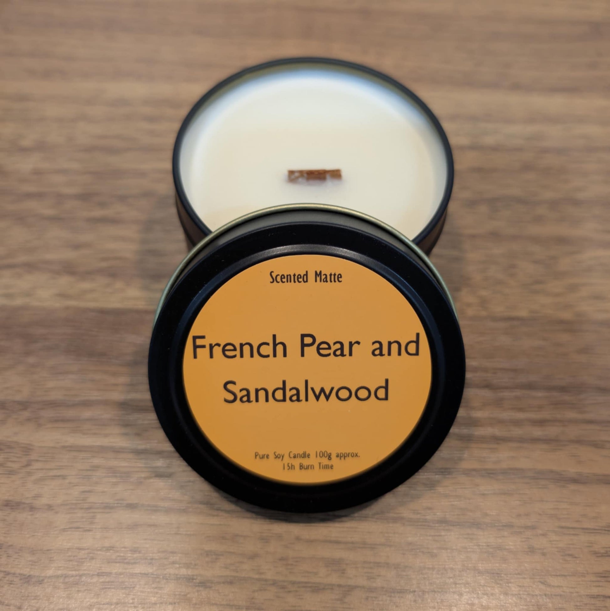 Scented candle in a black tin with 'French Pear and Sandalwood' label on a wooden surface
