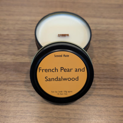Scented candle in a black tin with 'French Pear and Sandalwood' label on a wooden surface