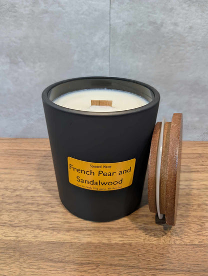 A soy wooden wick candle in a matte black glass jar with an orange label and wooden lid
