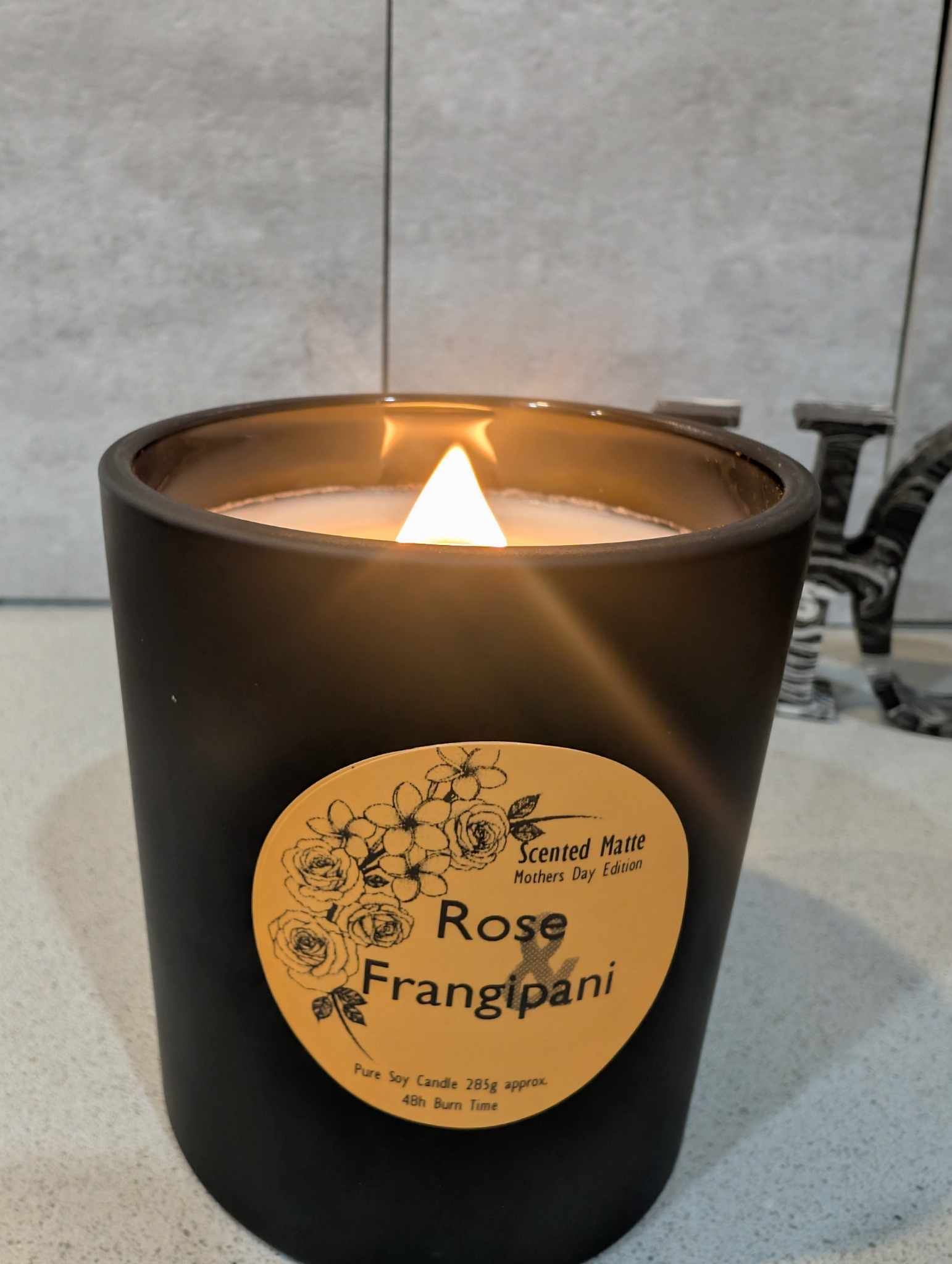 A matte black candle jar with orange label that's lit