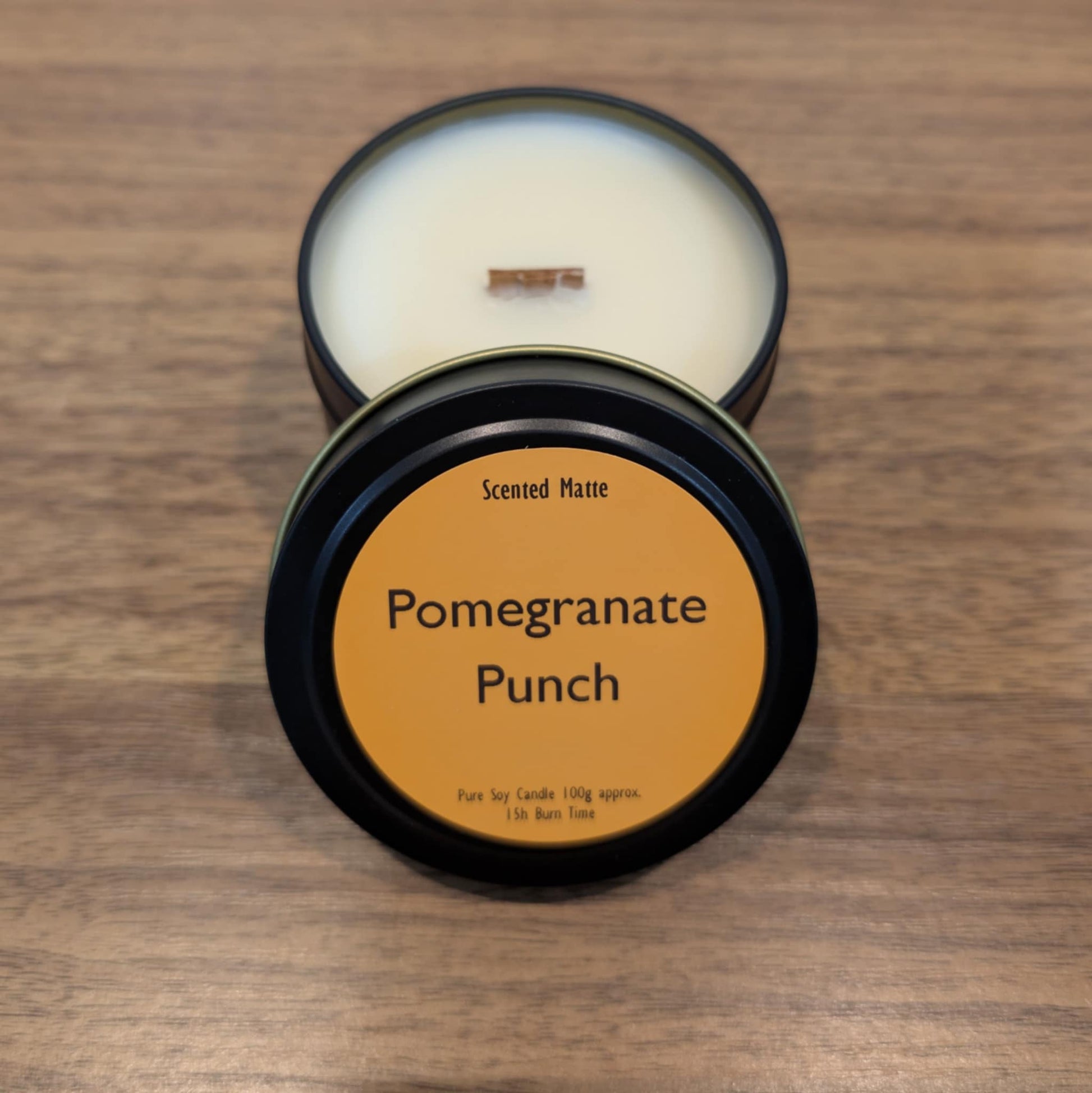 Scented candle in a black tin with 'Pomegranate Punch' label on a wooden surface