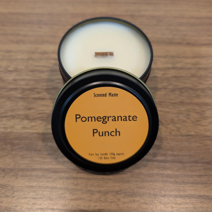 Scented candle in a black tin with 'Pomegranate Punch' label on a wooden surface