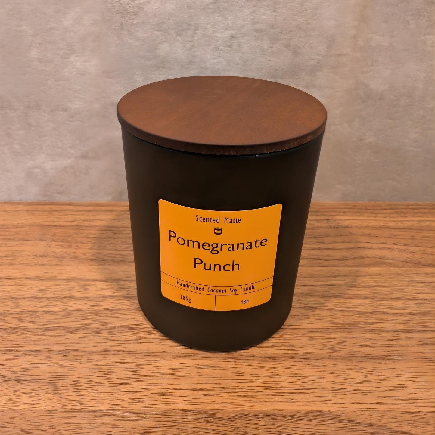 A minimalist matte black candle jar with a vibrant orange label and a dark wood lid.
