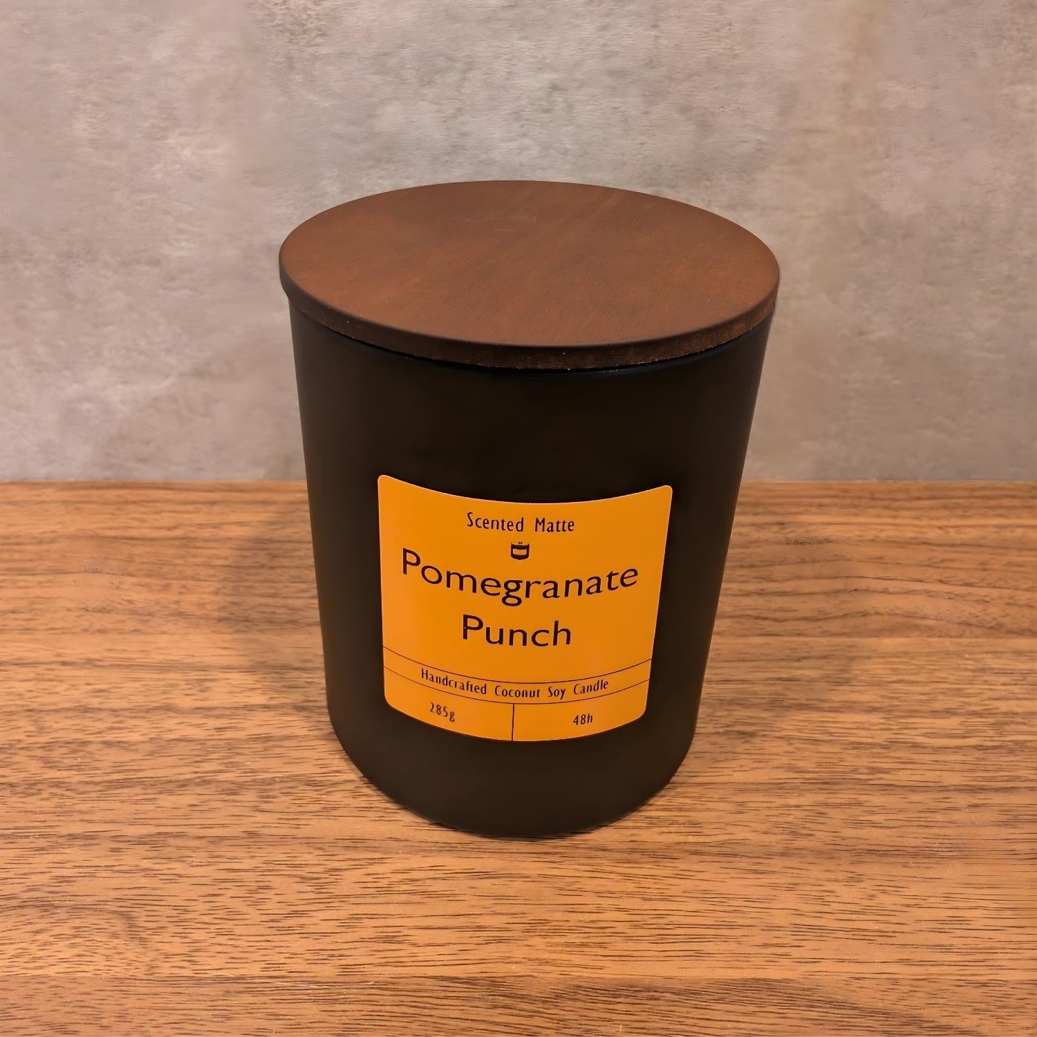 A minimalist matte black candle jar with a vibrant orange label and a dark wood lid.