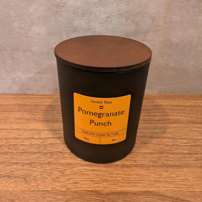 A minimalist matte black candle jar with a vibrant orange label and a dark wood lid.