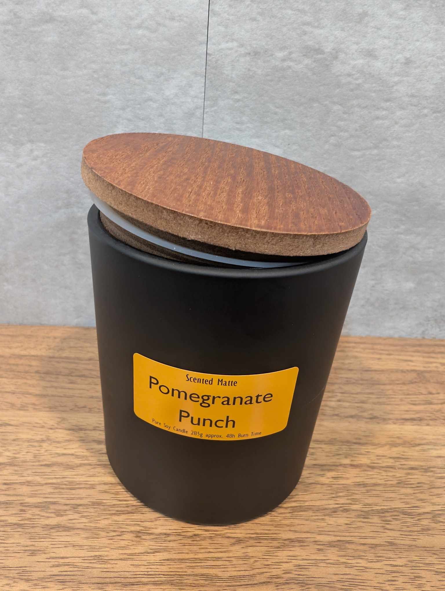 A matte black candle jar with orange label and a wooden lid on top