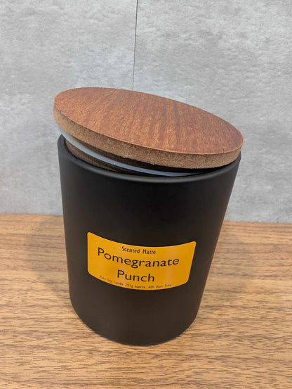 A matte black candle jar with orange label and a wooden lid on top