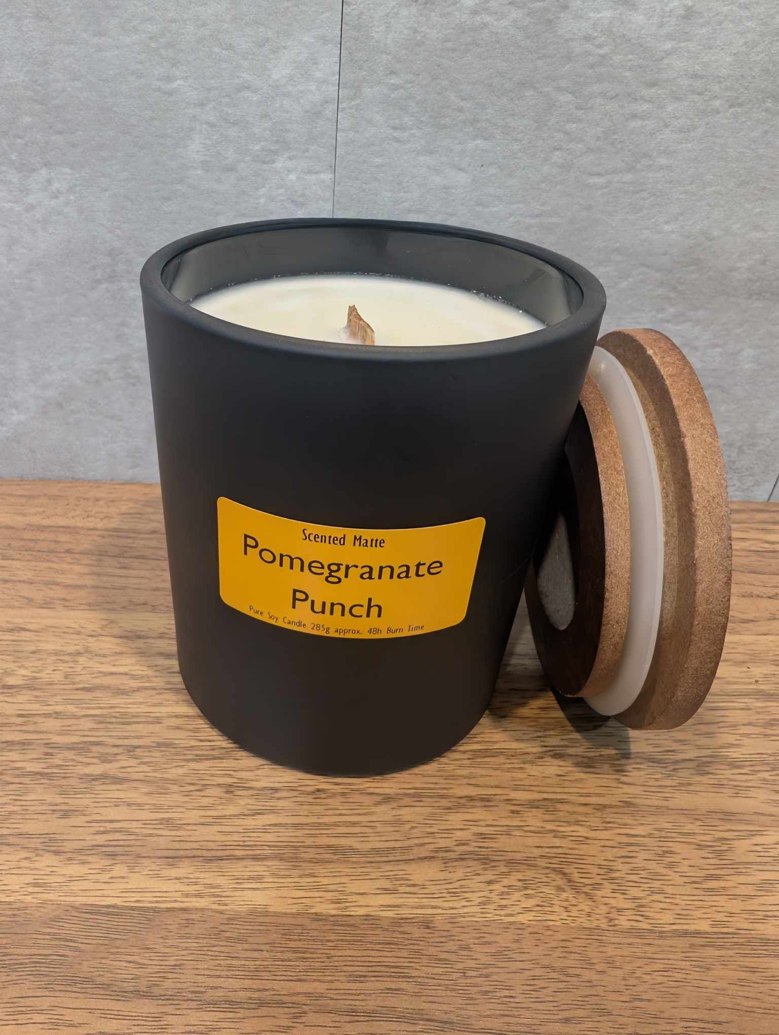 A soy wooden wick candle in a matte black glass jar with an orange label and wooden lid
