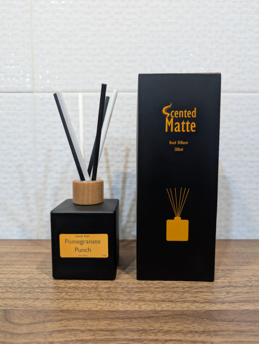 Matte black diffuser bottle with black and white reed sticks and wooden cap, next to its packaging on a wooden surface.