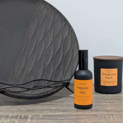 A matte black room spray bottle and a minimalist matte black candle jar, styled next to a large textured charcoal grey decorative plate.