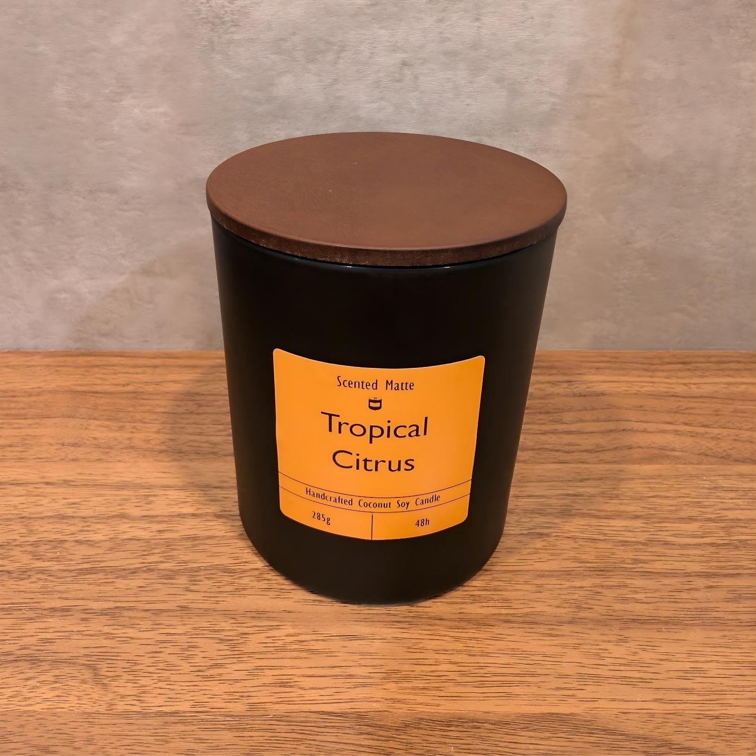 A minimalist matte black candle jar with a vibrant orange label and a dark wood lid.