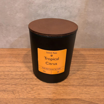 A minimalist matte black candle jar with a vibrant orange label and a dark wood lid.