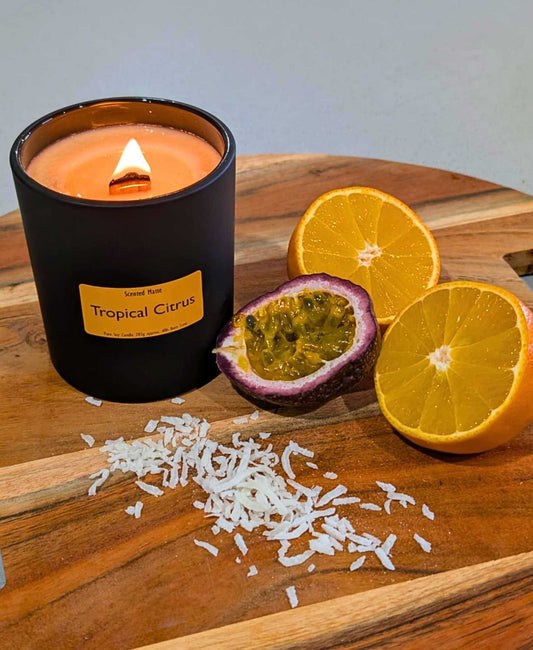 A cut open tangerine and passionfruit with shredded coconut and a lit wooden wick candle in a matte black jar