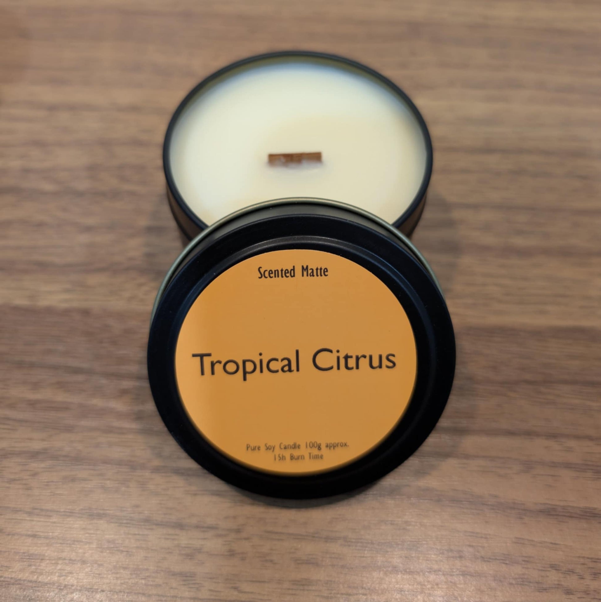 Scented candle in a black tin labeled 'Tropical Citrus' on a wooden surface