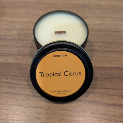Scented candle in a black tin labeled 'Tropical Citrus' on a wooden surface