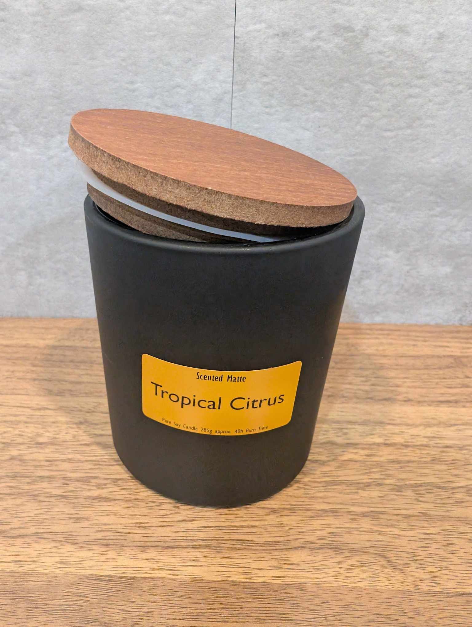 A matte black candle jar with orange label and a wooden lid on top