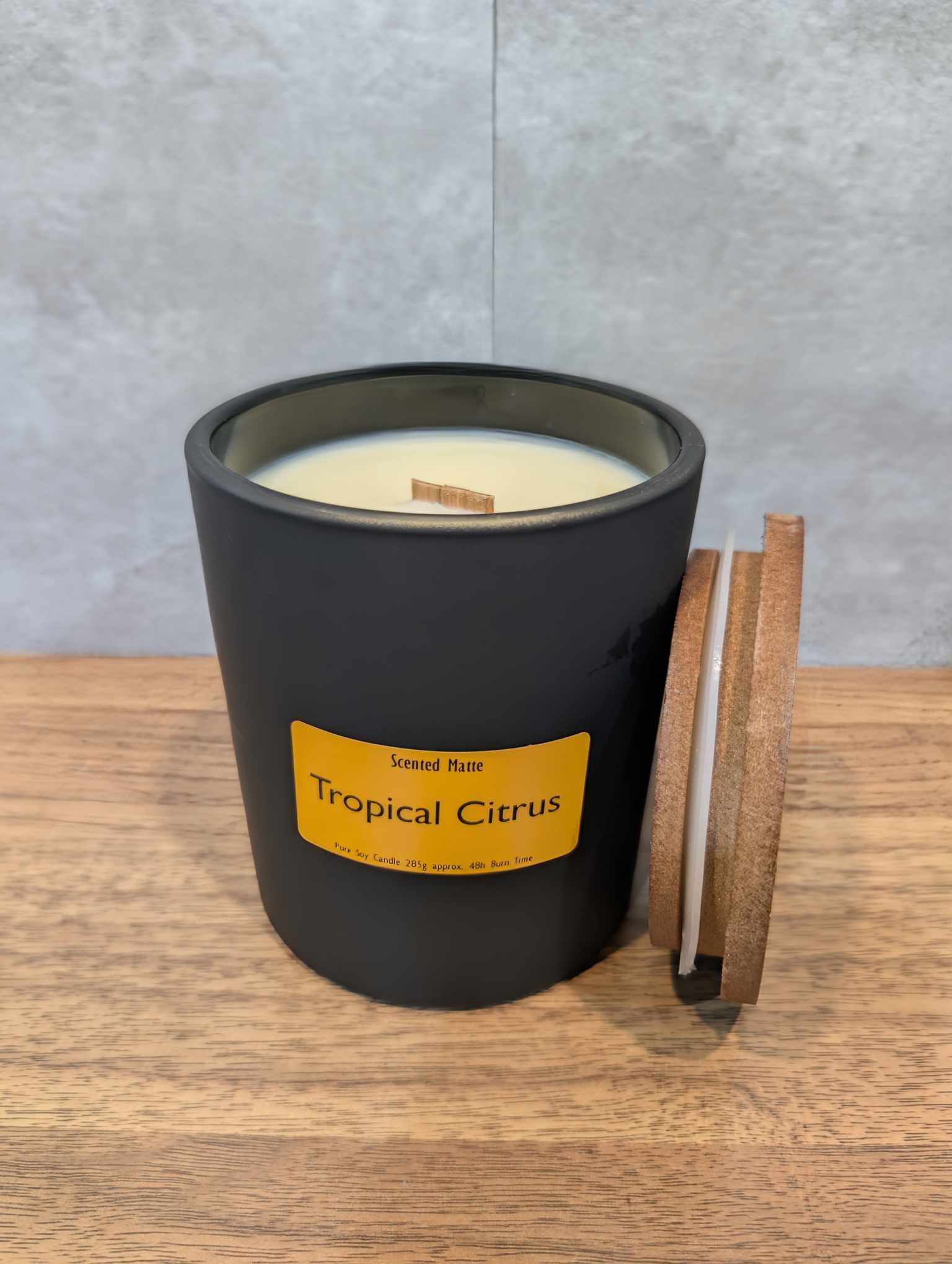 A soy wooden wick candle in a matte black glass jar with an orange label and wooden lid