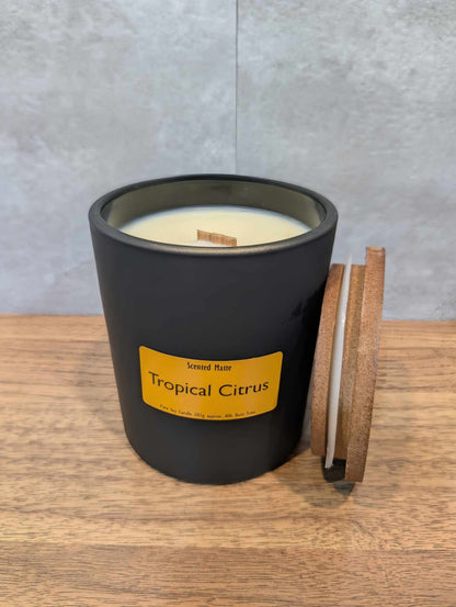 A soy wooden wick candle in a matte black glass jar with an orange label and wooden lid
