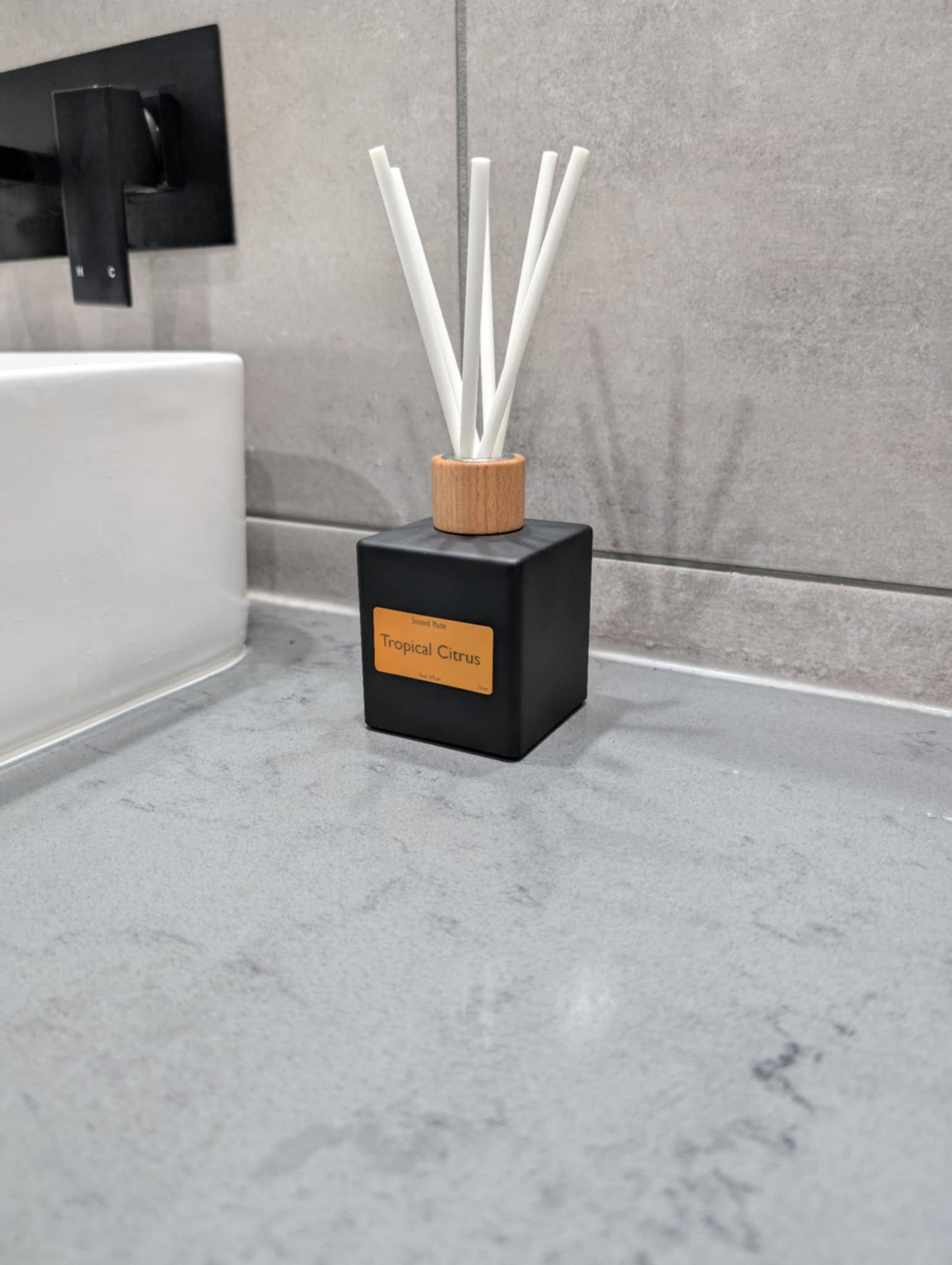 Black diffuser with wooden cap and white sticks on a gray bathroom counter